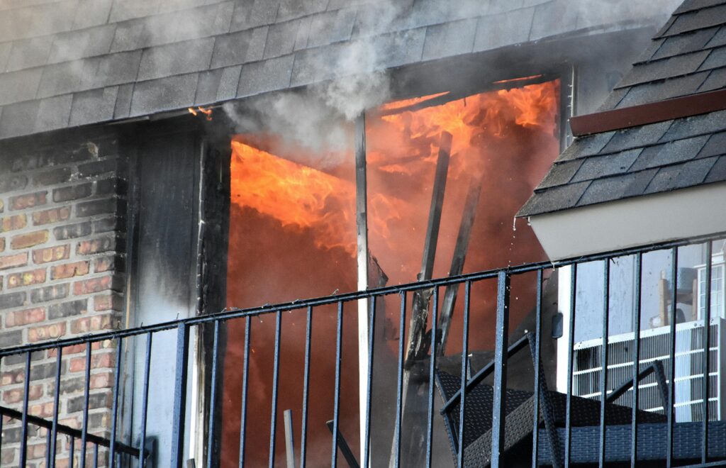 A blazing fire erupts from an apartment window, showcasing dramatic flames and smoke.